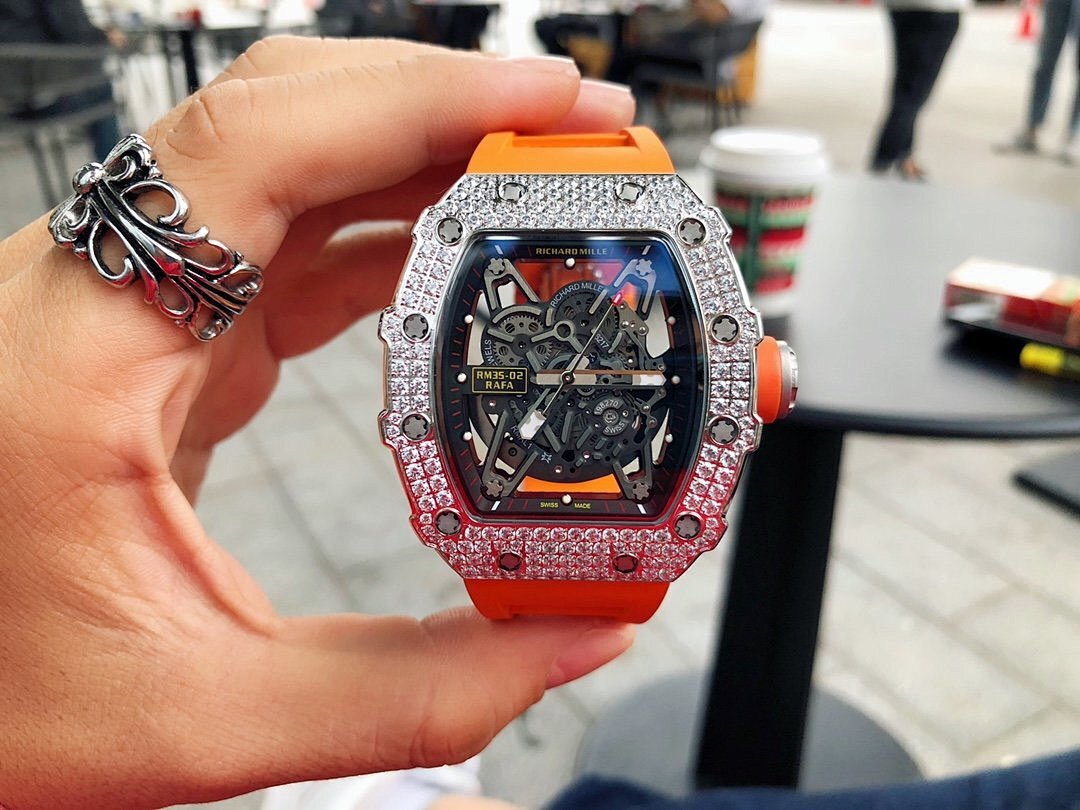 Richard Mille watch held up, silver gem-set bezel, red-orange rubber strap, detailed dial.
