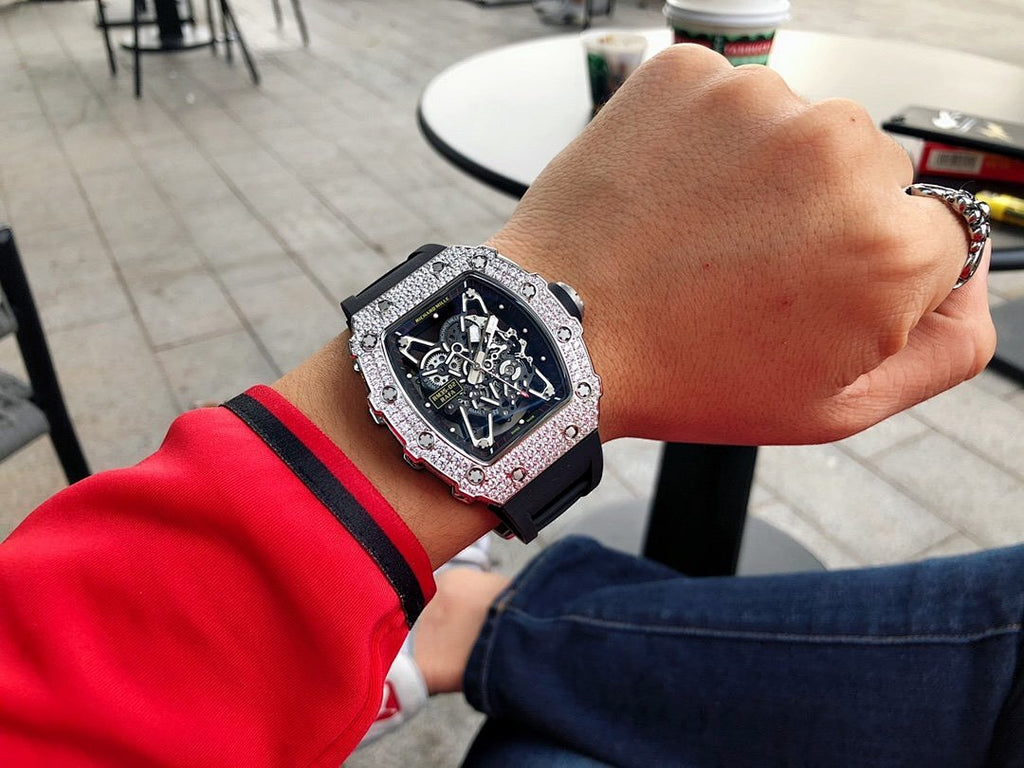 Richard Mille watch on wrist with silver gem-set bezel and black dial, black rubber strap.