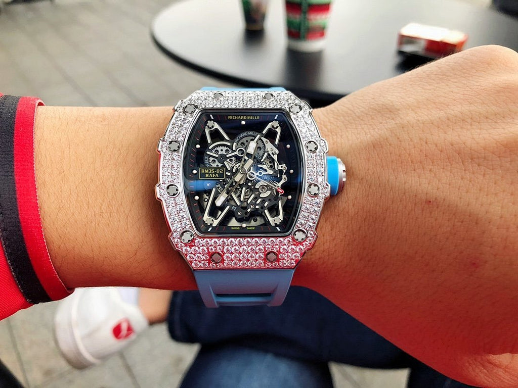 Richard Mille watch on wrist with silver gem-set bezel and blue rubber strap.