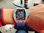 Richard Mille watch on wrist with silver gem-set bezel and blue rubber strap.