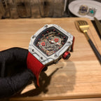 Square luxury watch with red rubber strap, white case, and exposed mechanical dial.