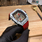Square luxury watch with red strap and white case, skeleton dial with red accents.