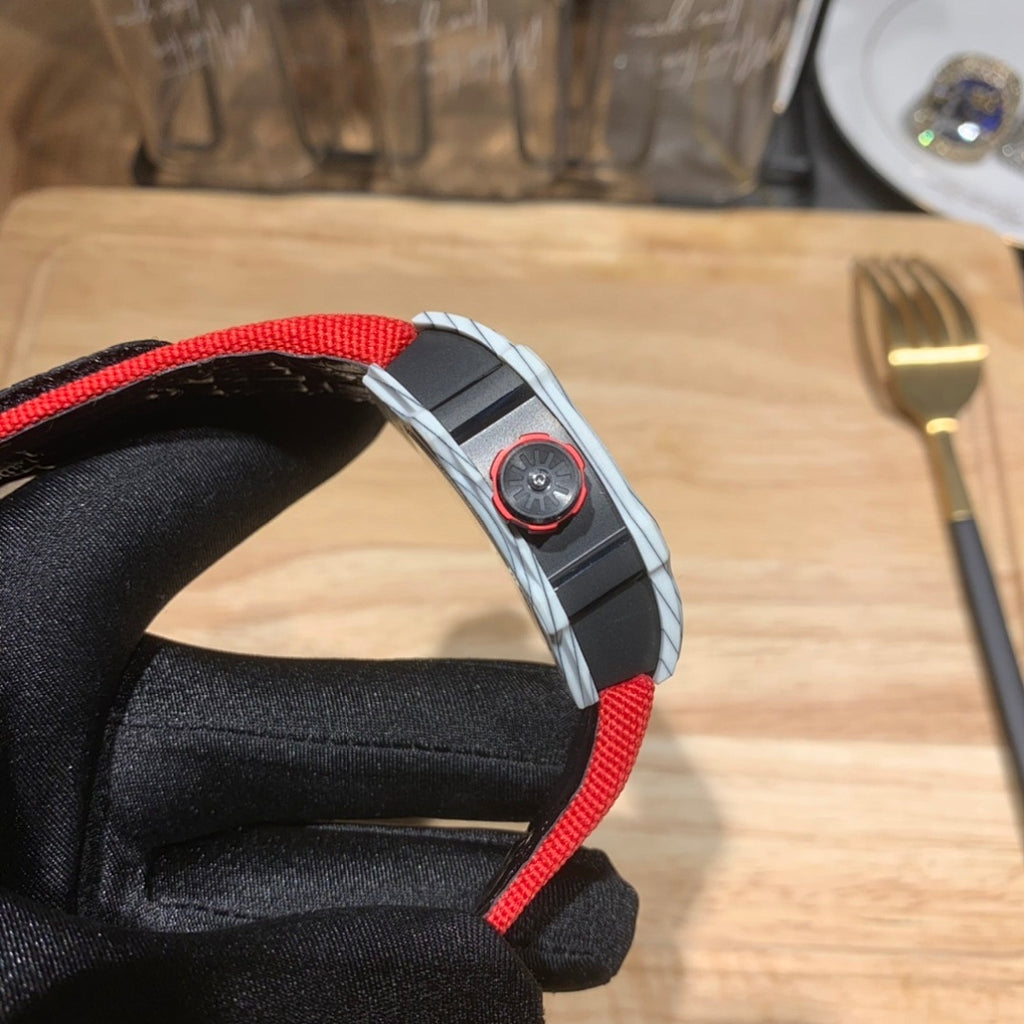 Square luxury watch case side with red strap, visible bezel details and crown element.