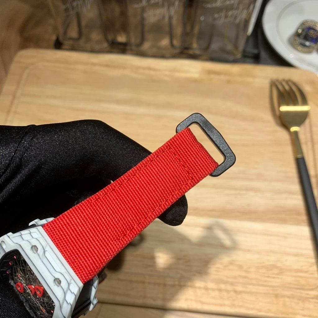 Red fabric strap looped through watch case, shown from above with black case edge.