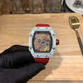 Square luxury watch with red dial accents, white case, and red rubber strap.