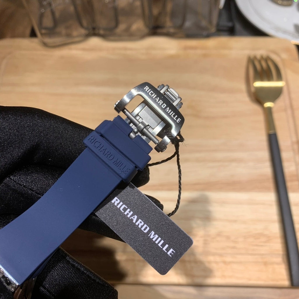 Richard Mille watch with blue strap, silver clasp, and dangling fabric tag