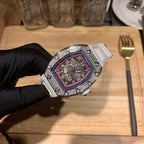 Luxury watch with white strap, jeweled bezel, red-blue skeleton dial angled view
