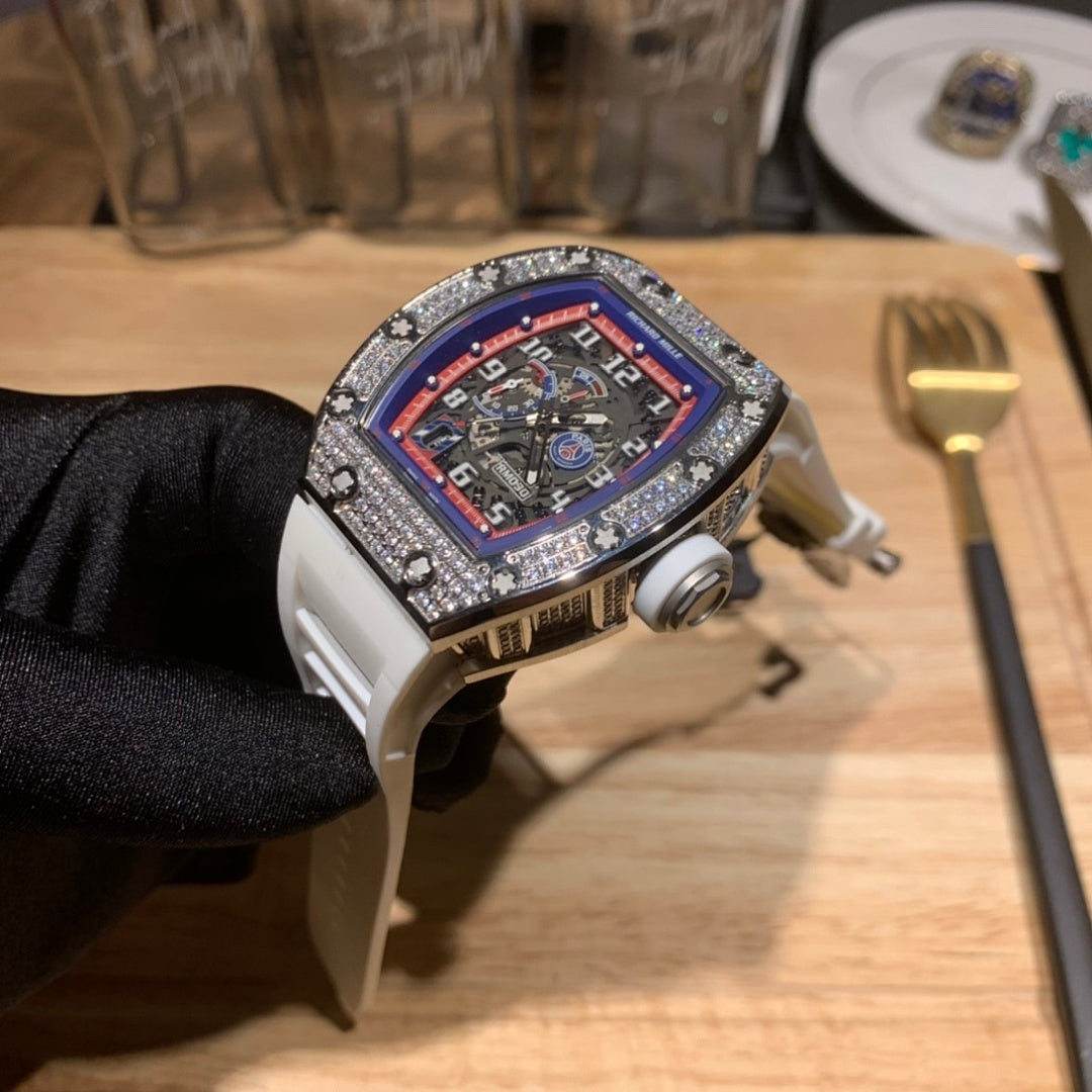Luxury watch with white strap, jeweled bezel, red-blue dial, 3/4 side angle