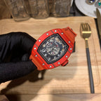 Orange watch with black dial detail, close side angle held by black glove