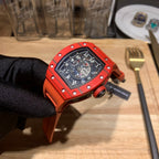 Orange watch with black dial and strap, angled view held by gloved hand