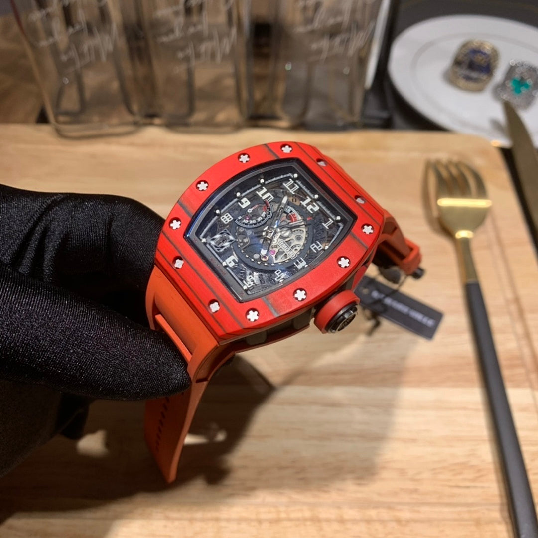 Orange watch with black dial and strap, angled view held by gloved hand