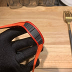 Orange watch case with black textured strap, close-up from the side