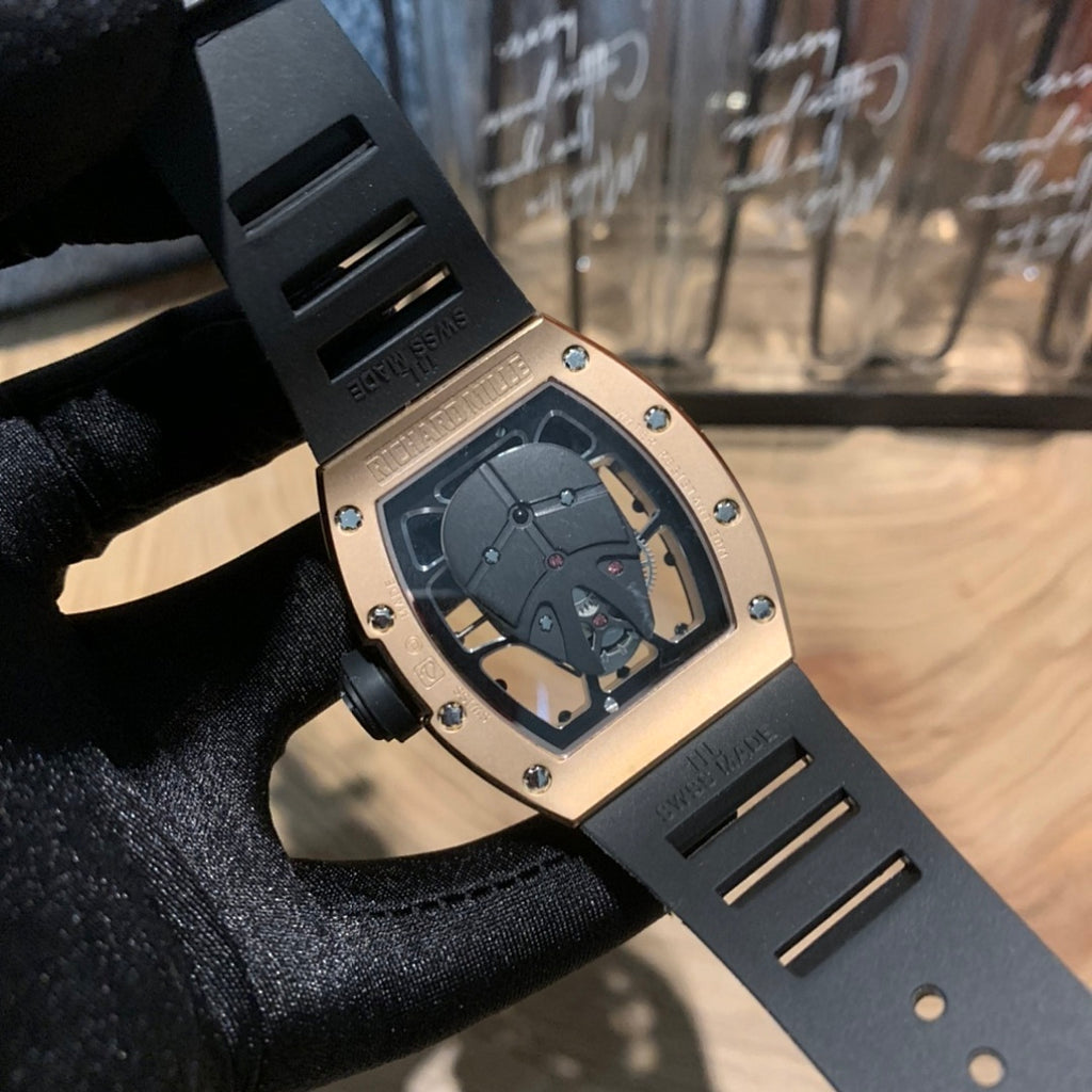 Rose gold-toned square watch with black strap and jeweled bezel, skeleton dial