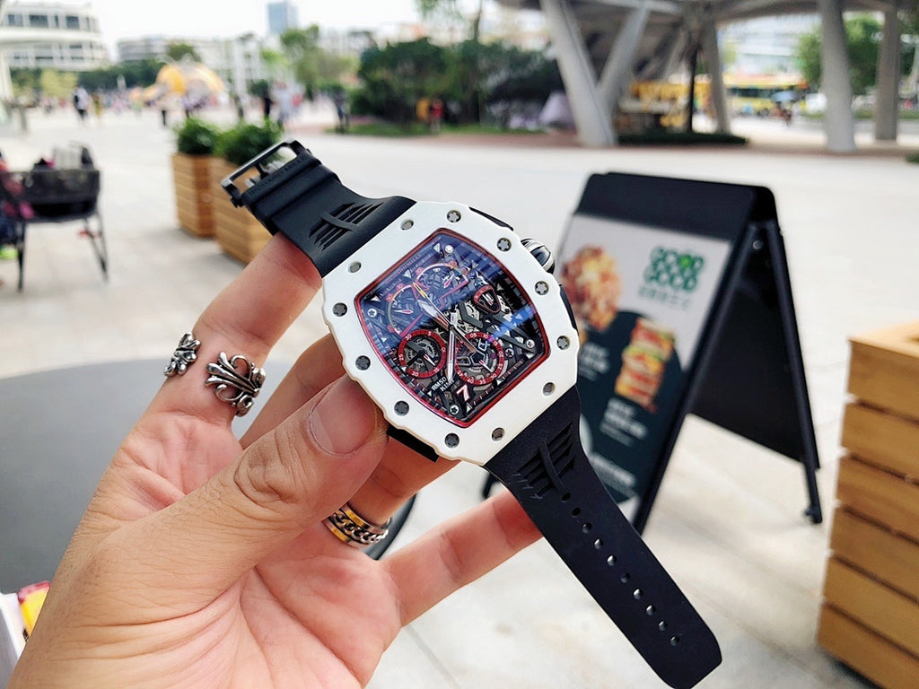 Richard Mille wristwatch held up, white case and black strap, skeleton dial with red border