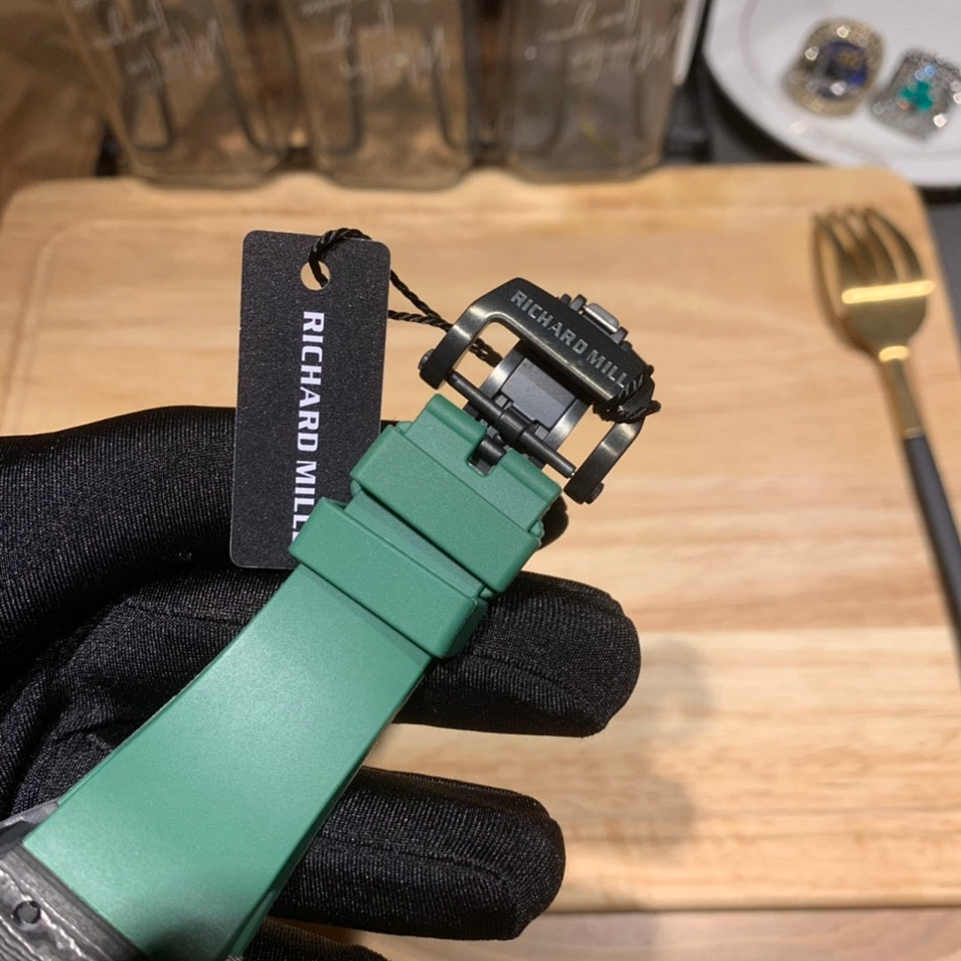 Watch with green rubber strap and dark buckle clasp, shown on a gloved hand with tag