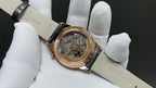 Open-work gold dial dress watch with star detail, black leather strap on white gloves.