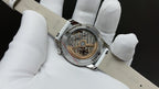 Vacheron Constantin watch showing mechanical movement through open dial, white leather strap