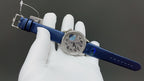 Luxury wristwatch with blue leather strap and visible buckle hardware on white gloves