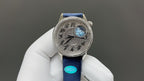 Luxury wristwatch with blue leather strap and ornate silver dial with blue globe detail