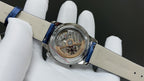 Luxury wristwatch with blue leather strap, open caseback showing mechanical movement
