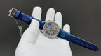 Round watch with blue leather strap, silver case and blue dial, shown on gloved hand