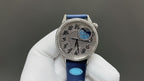 Round watch on blue leather strap, ornate silver case and blue dial with central motif