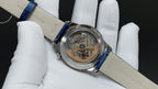 Round skeleton watch with blue leather strap, silver case, visible gears under glass
