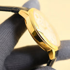 Gold-tone wristwatch with a polished case and black leather strap.