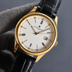 Gold wristwatch with white dial, black leather strap, and date window showing 15