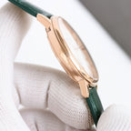 Rose-gold wristwatch with green leather strap and crown, side view on white cushion