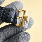 Black leather watch strap with gold buckle and clasp, end piece on gray glove