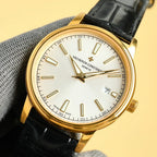 Gold wristwatch with white dial and black leather strap, date at 7 o'clock