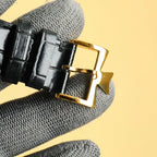 Gold watch clasp with black leather strap and buckle detail