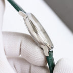Silver-tone wristwatch case with green leather strap and crown, side profile