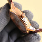 Wristwatch rose-gold side profile with crown, on brown leather strap.
