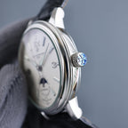 Automatic wristwatch crown with blue emblem, silver case, cream dial, black strap