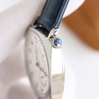 Wristwatch case side view with blue leather strap and crown, with glass reflecting light