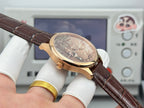 Gold-tone wristwatch with brown leather strap and crown, round dial with Eiffel Tower scene