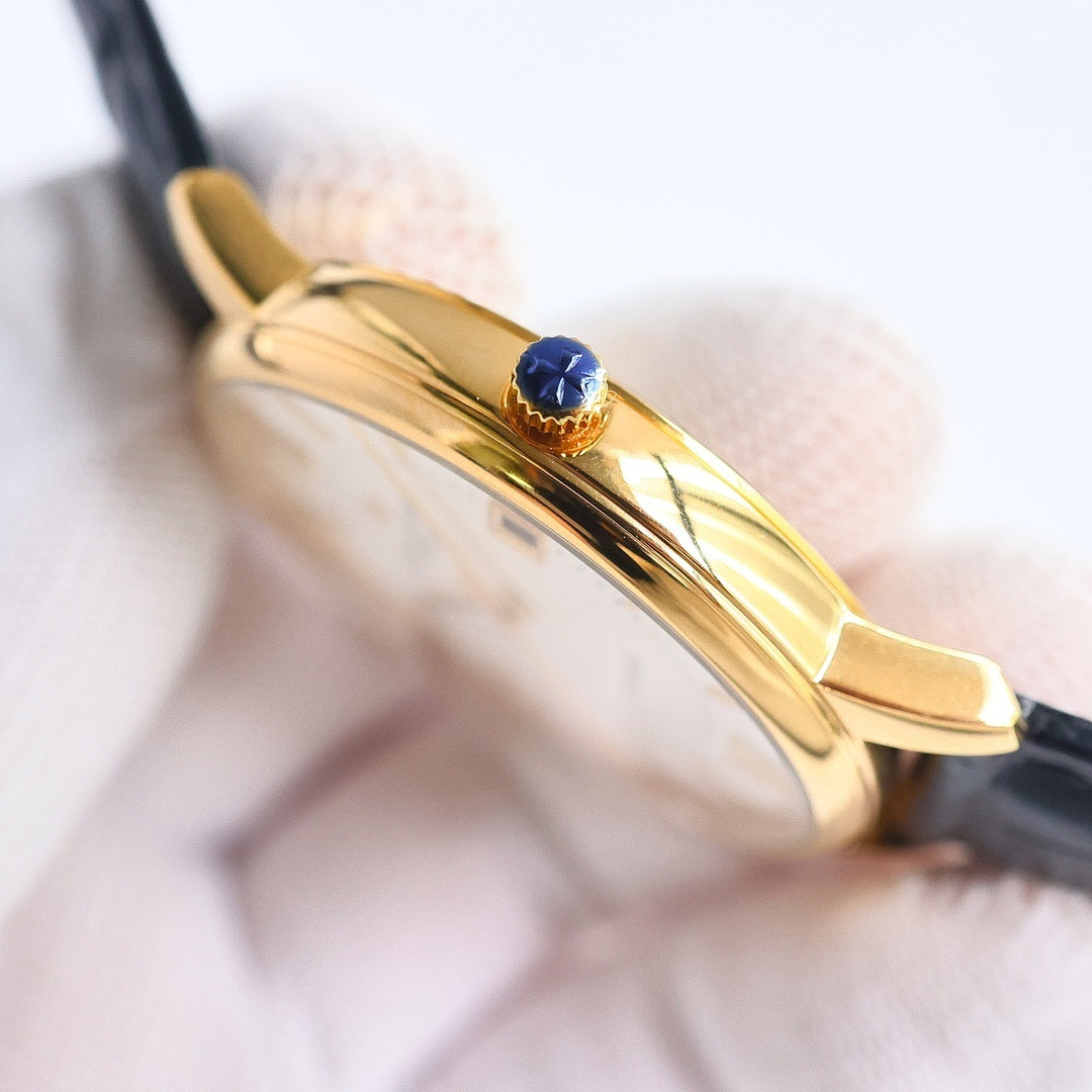 Gold watch case side with blue gemstone crown, black leather strap