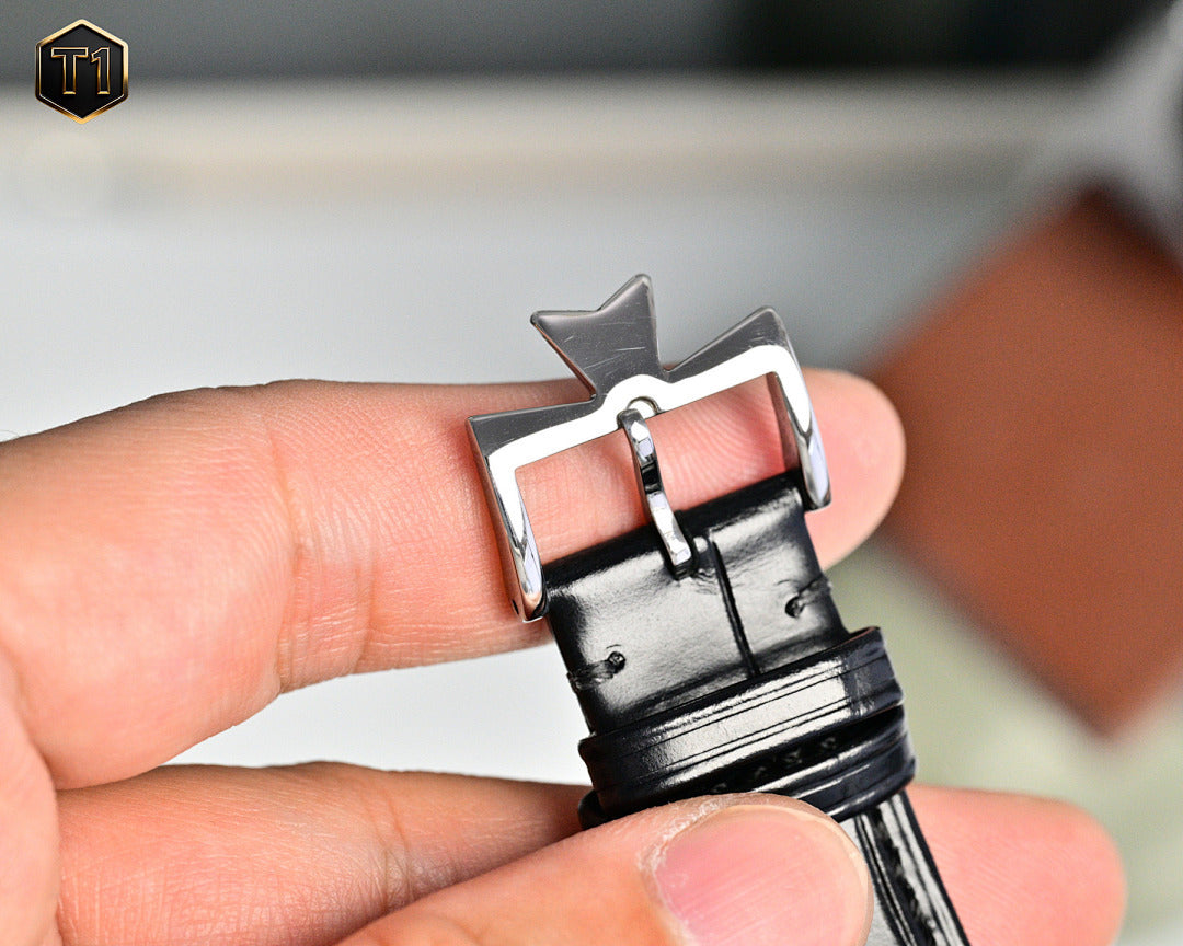 Stainless steel watch buckle with black leather strap, clasp detail held in hand.