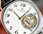 Stainless steel watch face with white dial, roman numerals, and exposed balance wheel.