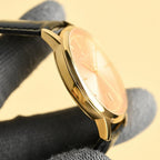 Luxury wristwatch side profile with pale dial, gold case, and black leather strap