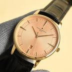 Luxury wristwatch with pink dial, gold case, black leather strap and date window