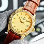 Gold-tone watch with yellow dial, brown leather strap, jeweled bezel, date window at 6