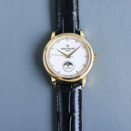 Gold wristwatch with white dial and black leather strap; baton hour markers.