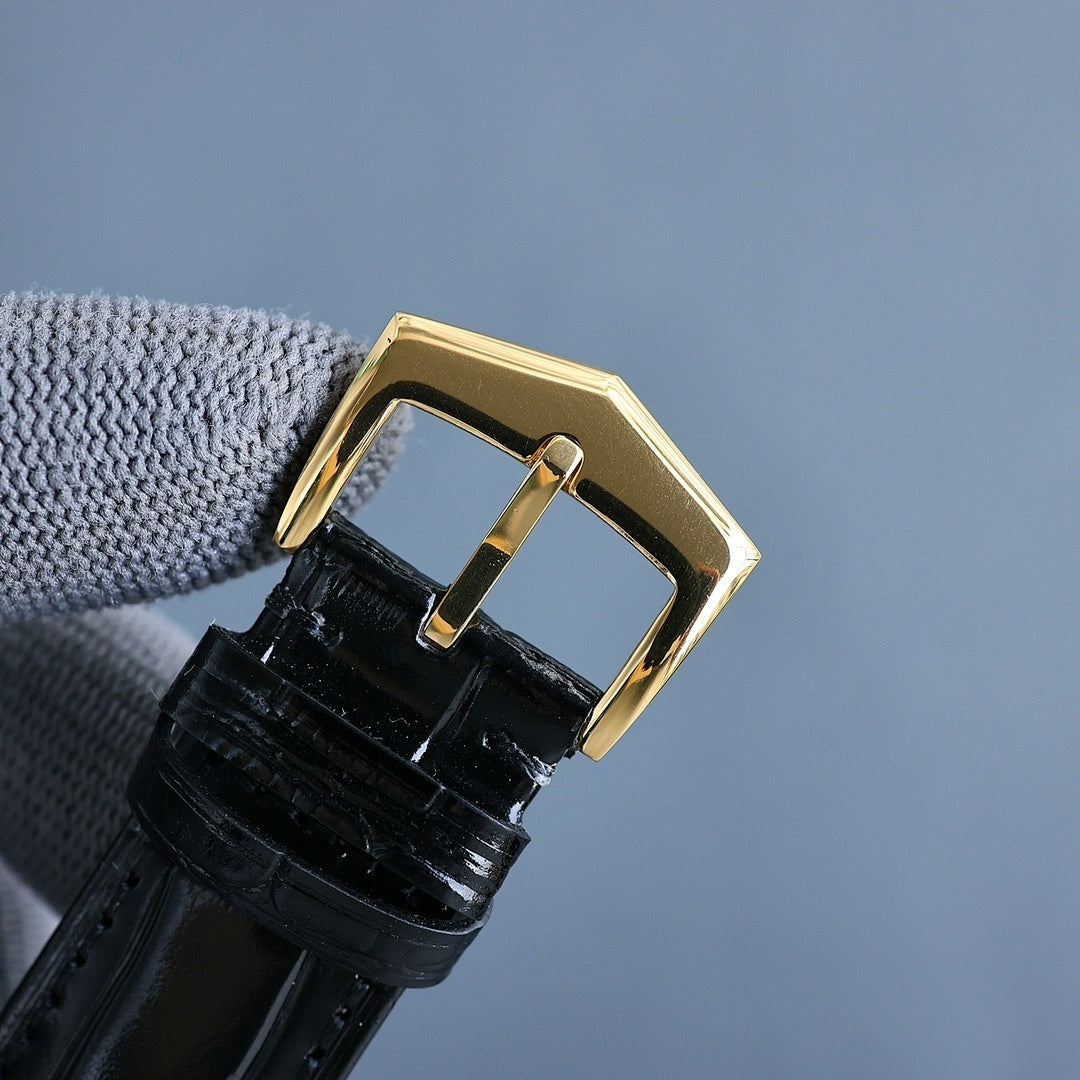 Gold wristwatch case with black leather strap; angled side view with crown.