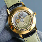 Gold-tone caseback showing mechanical watch movement and patterned engravings, black leather strap.