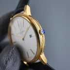 Vacheron Constantin wristwatch side: gold case, black strap, blue crown, white dial.