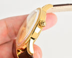 Gold-tone wristwatch side view with crown and brown leather strap