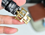 Black leather watch strap with gold-tone deployant clasp, wristwatch close-up